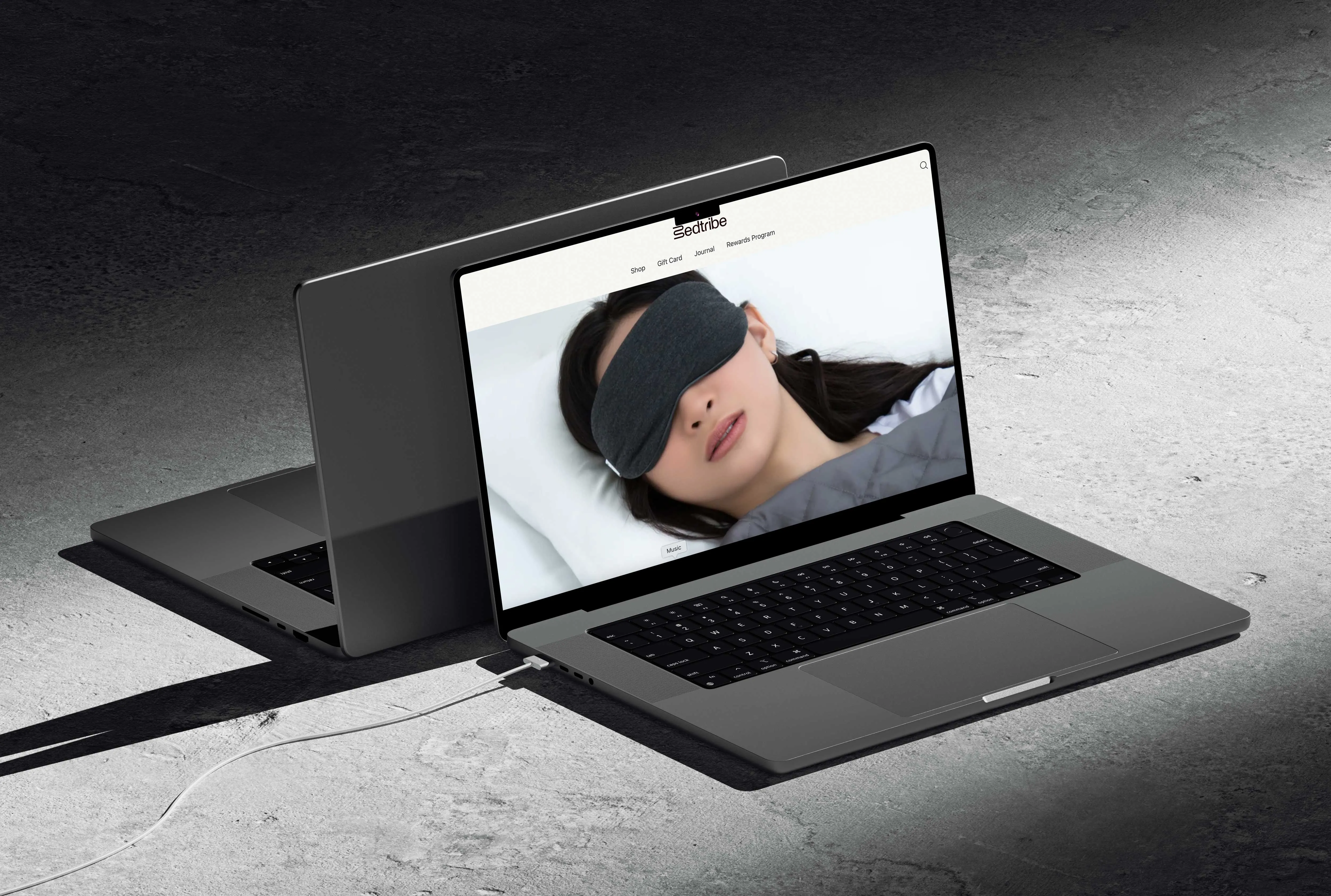 Laptop on concrete showing the Bedtribe homepage with a woman in a sleep mask