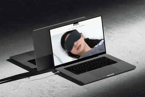 Laptop on concrete showing the Bedtribe homepage with a woman in a sleep mask