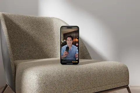 Phone showing a TikTok creator video, propped on a boucle armchair